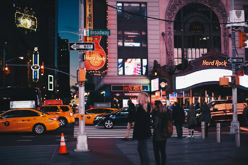 NYC Broadway street at night with yellow taxis, traffic cones, and pedestrians.